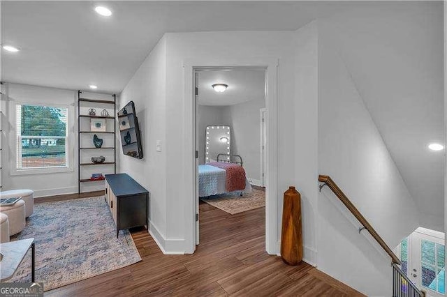 hallway featuring baseboards, wood finished floors, an upstairs landing, and recessed lighting