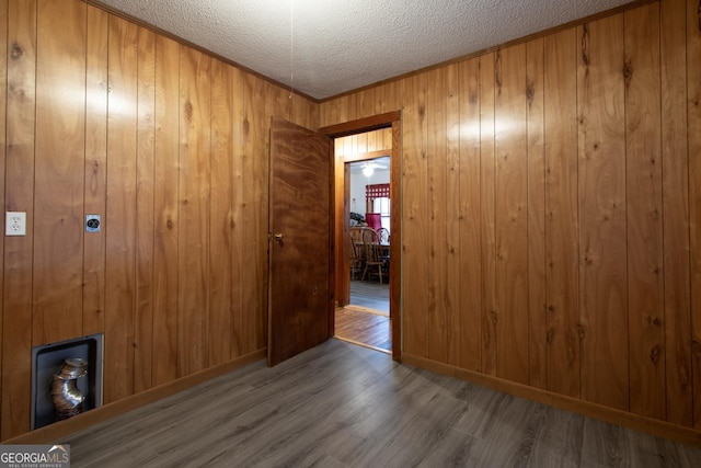 unfurnished room featuring wood-type flooring, ornamental molding, wooden walls, and a textured ceiling