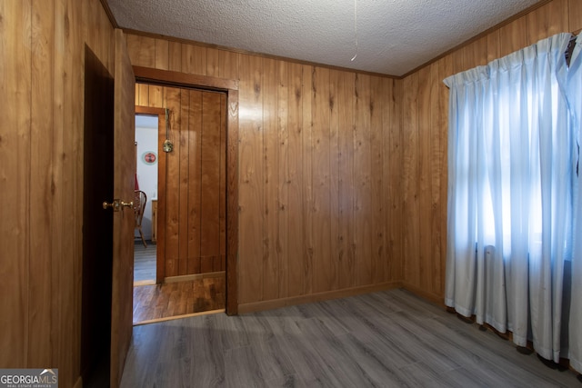 empty room featuring crown molding, wood-type flooring, a textured ceiling, and wood walls