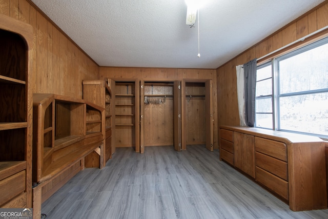 interior space with a textured ceiling, light hardwood / wood-style floors, and wood walls