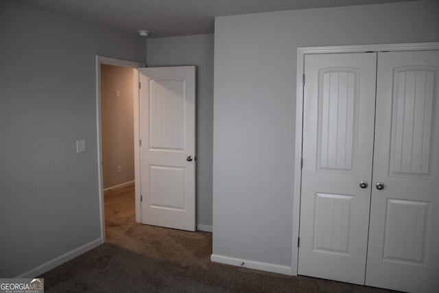 unfurnished bedroom with dark carpet and a closet