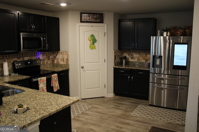 kitchen with tasteful backsplash, appliances with stainless steel finishes, light stone countertops, and light hardwood / wood-style flooring