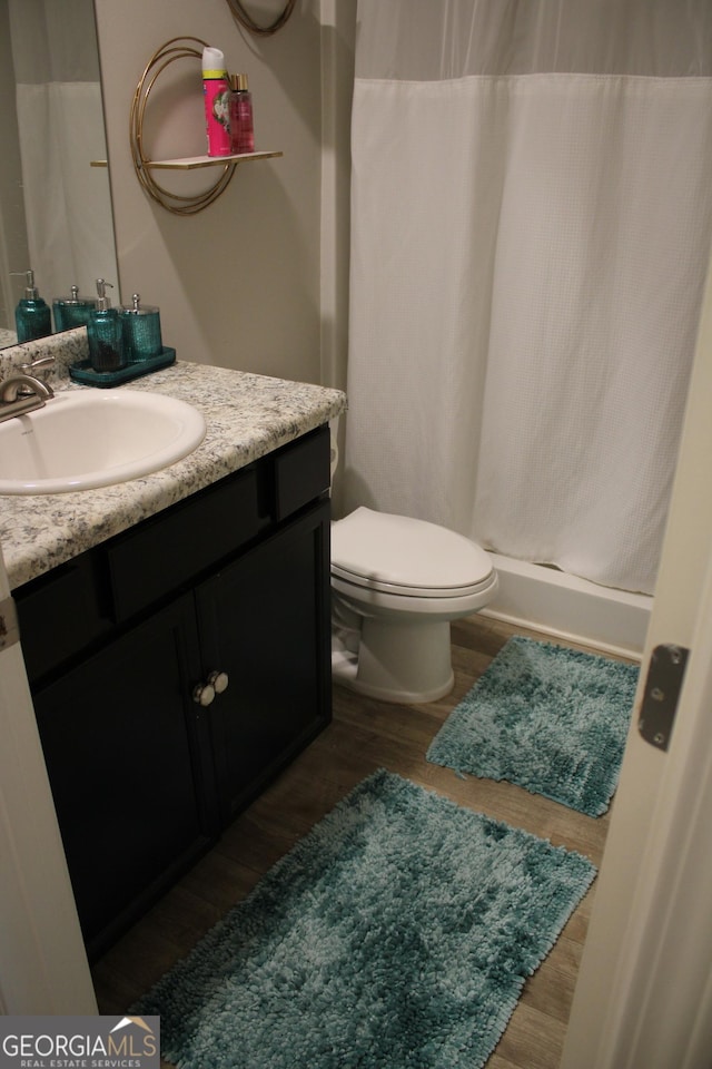 bathroom featuring hardwood / wood-style flooring, vanity, toilet, and curtained shower