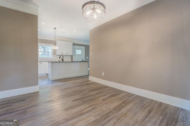 unfurnished living room featuring sink, an inviting chandelier, and light wood-type flooring