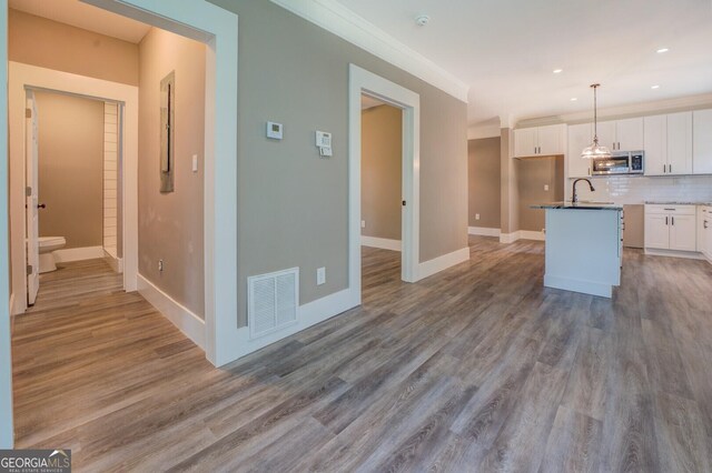 kitchen with decorative light fixtures, light wood-type flooring, white cabinets, a kitchen island with sink, and backsplash