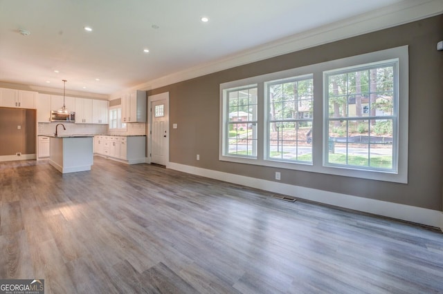 unfurnished living room with ornamental molding, plenty of natural light, sink, and hardwood / wood-style floors