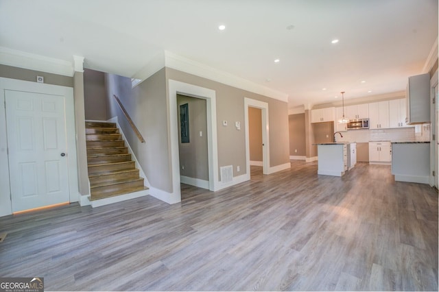 unfurnished living room with sink, ornamental molding, and light hardwood / wood-style floors