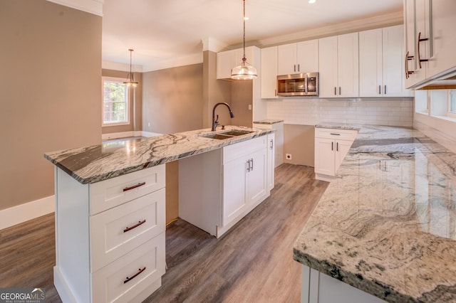 kitchen featuring sink, hanging light fixtures, white cabinets, and a center island with sink