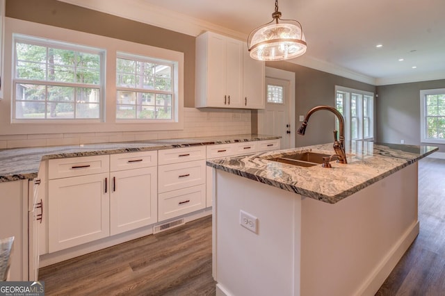 kitchen featuring white cabinetry, sink, hanging light fixtures, ornamental molding, and a center island with sink