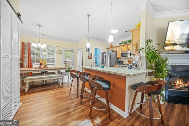 kitchen featuring a breakfast bar, appliances with stainless steel finishes, decorative backsplash, decorative light fixtures, and light brown cabinets