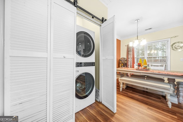 washroom with hardwood / wood-style floors, stacked washer and clothes dryer, ornamental molding, a barn door, and a chandelier