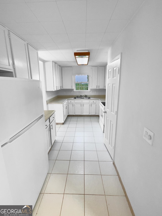 kitchen with light tile patterned floors, white appliances, sink, white cabinets, and a drop ceiling