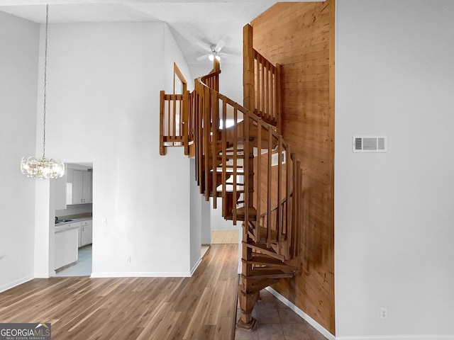 stairs featuring hardwood / wood-style flooring, ceiling fan with notable chandelier, and wood walls