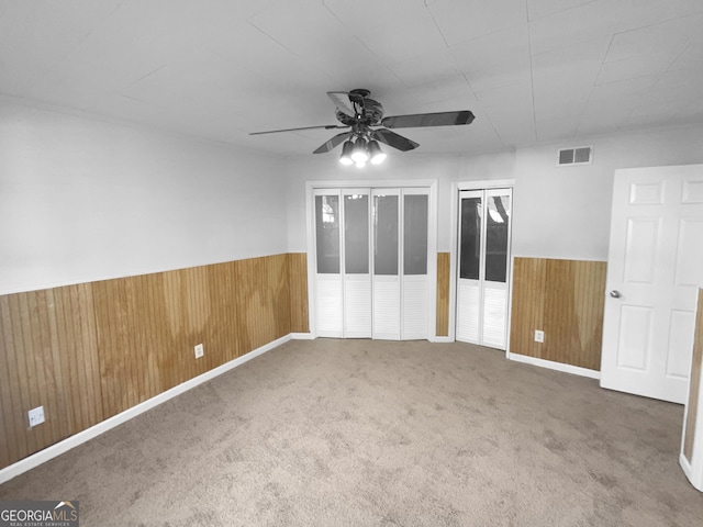 carpeted spare room with ceiling fan and wooden walls