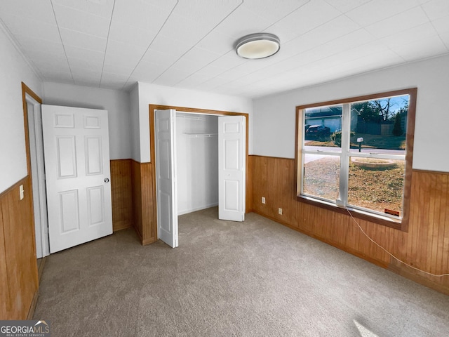 unfurnished bedroom featuring carpet floors, wooden walls, and a closet