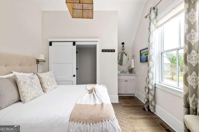 bedroom featuring visible vents, a barn door, vaulted ceiling, wood finished floors, and baseboards