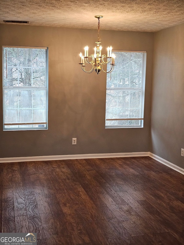 unfurnished dining area with dark hardwood / wood-style flooring, a textured ceiling, and an inviting chandelier