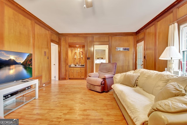 living room with ornamental molding, wooden walls, ceiling fan, and light wood-type flooring