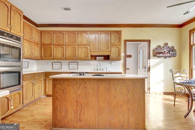 kitchen featuring crown molding, a kitchen island, double oven, and light hardwood / wood-style flooring