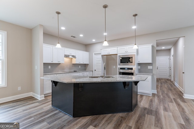 kitchen featuring built in microwave, light stone countertops, oven, a kitchen island with sink, and white cabinets