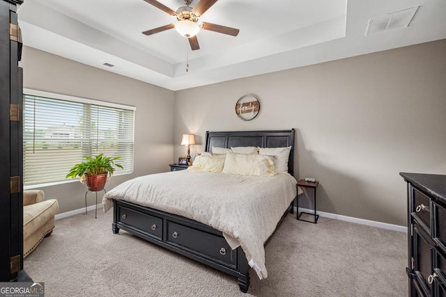 carpeted bedroom with ceiling fan and a tray ceiling