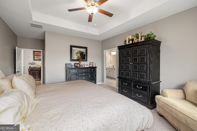 carpeted bedroom featuring connected bathroom, a tray ceiling, and ceiling fan