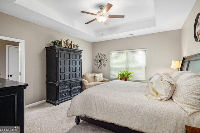 bedroom with light colored carpet, baseboards, a tray ceiling, and a ceiling fan