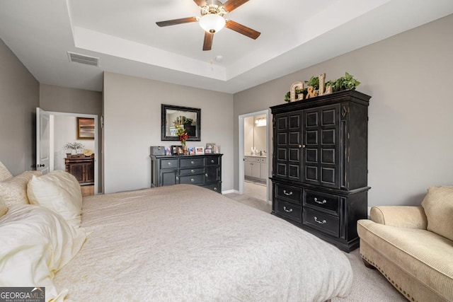 bedroom with visible vents, ensuite bathroom, a raised ceiling, light colored carpet, and ceiling fan