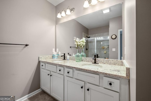 full bathroom with a shower stall, double vanity, baseboards, and a sink