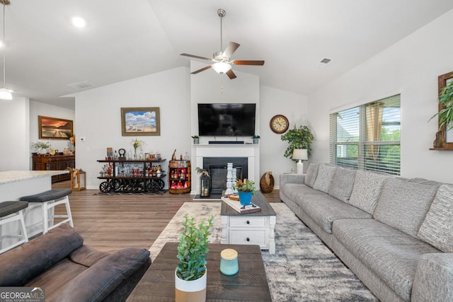 living room with visible vents, a ceiling fan, a glass covered fireplace, wood finished floors, and vaulted ceiling