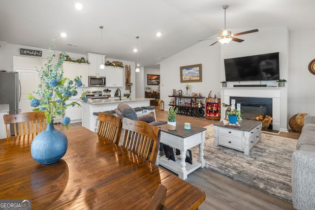 living area with a glass covered fireplace, ceiling fan, vaulted ceiling, and light wood finished floors