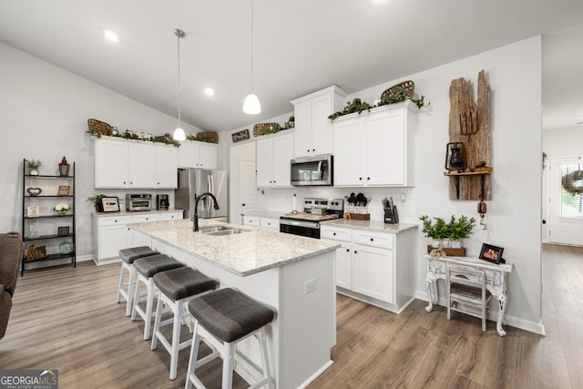 kitchen with sink, white cabinets, light stone counters, stainless steel appliances, and a center island with sink