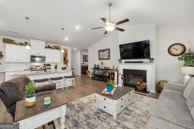 living room featuring visible vents, ceiling fan, vaulted ceiling, and light wood finished floors