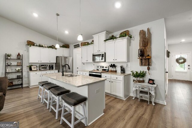 kitchen featuring a center island with sink, appliances with stainless steel finishes, a kitchen breakfast bar, wood finished floors, and a sink