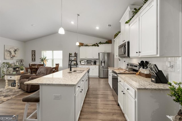 kitchen with wood finished floors, a sink, stainless steel appliances, white cabinets, and a kitchen bar