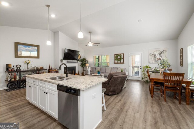 kitchen with light wood-style flooring, an island with sink, a sink, a fireplace, and dishwasher