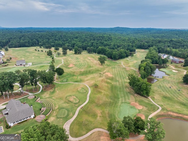 drone / aerial view with a water view, a wooded view, and golf course view