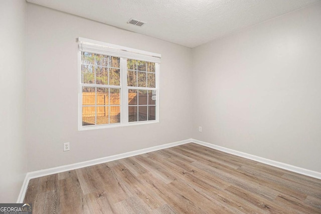 empty room with a textured ceiling and light hardwood / wood-style flooring