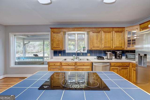 kitchen with tasteful backsplash, sink, light wood-type flooring, and appliances with stainless steel finishes