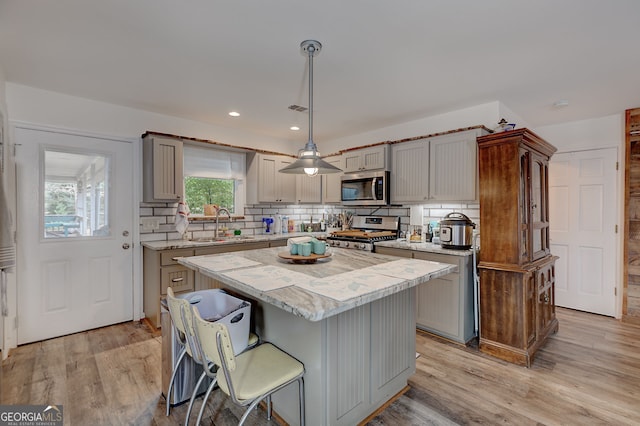 kitchen with a kitchen island, appliances with stainless steel finishes, pendant lighting, sink, and light wood-type flooring