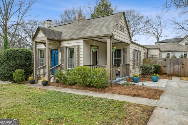 view of front of property featuring a yard, roof with shingles, fence, and a chimney