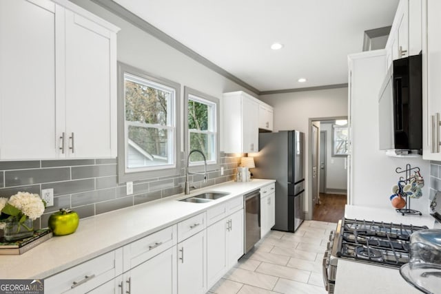 kitchen with appliances with stainless steel finishes, tasteful backsplash, white cabinetry, sink, and ornamental molding