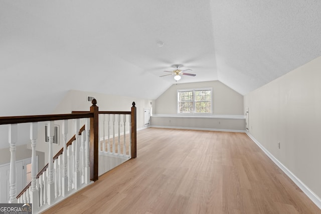 additional living space featuring ceiling fan, vaulted ceiling, a textured ceiling, and light wood-type flooring