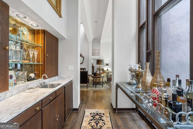 bar with dark wood-type flooring, stainless steel dishwasher, sink, and a high ceiling