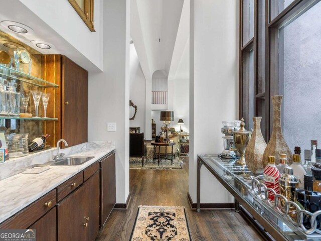 bar with baseboards, a sink, bar area, and dark wood-style floors