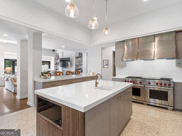 kitchen with range hood, double oven range, modern cabinets, a sink, and an island with sink