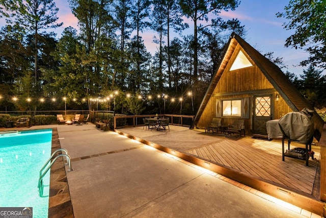 pool at dusk with an outdoor structure and a deck