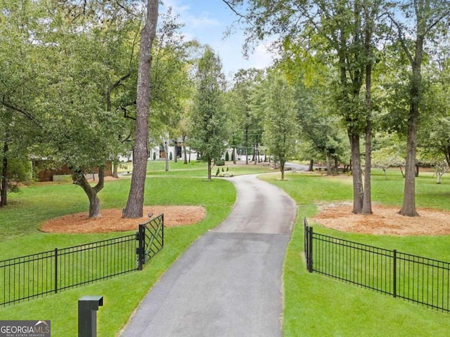 view of community with a yard, fence, and aphalt driveway