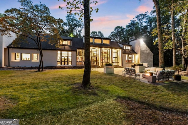 back house at dusk with an outdoor living space, a patio, and a lawn