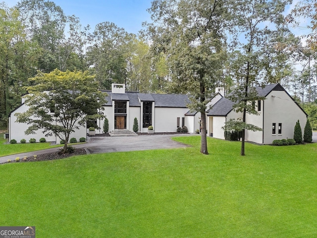 view of front of house featuring a shingled roof, stucco siding, driveway, and a front yard